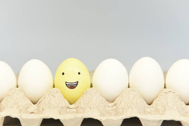 Laughing face emoticon grinning from ear to ear Illustration of a yellow laughing face emoticon on an egg shell with its mouth open surrounded by other white egg shells in an egg tray. sabby stock pictures, royalty-free photos & images