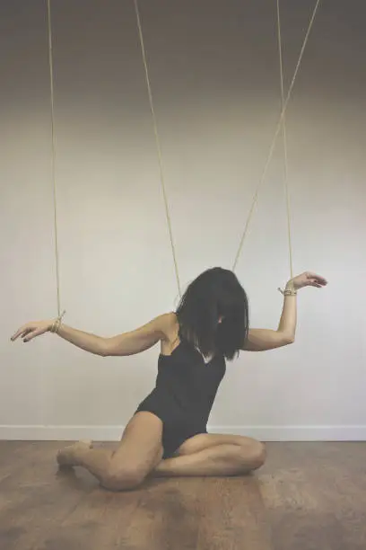Photo of tied woman puppet controlled by ropes, concept of control