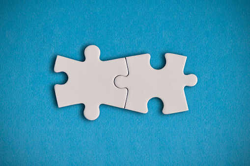 Two white jigsaw puzzle pieces on the blue background. Horizontal composition with enough copy space for your text.