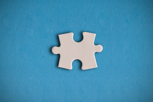 White jigsaw puzzle piece on the blue background. Horizontal composition with enough copy space for your text.