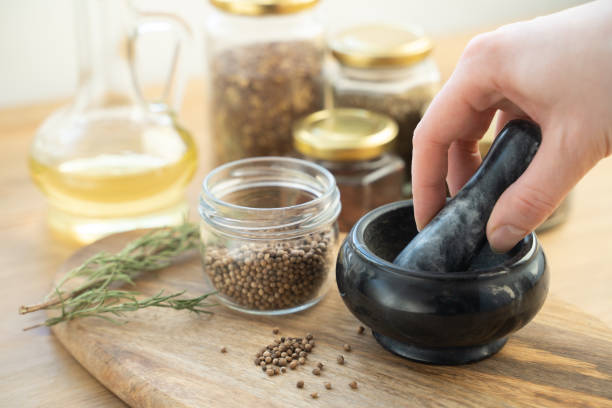 coriandolo intero secco schiacciato in polvere in una cucina tradizionale utilizzando malta di pietra smerigliatrice vintage e pestello - mortar and pestle herb coriander seed cilantro foto e immagini stock