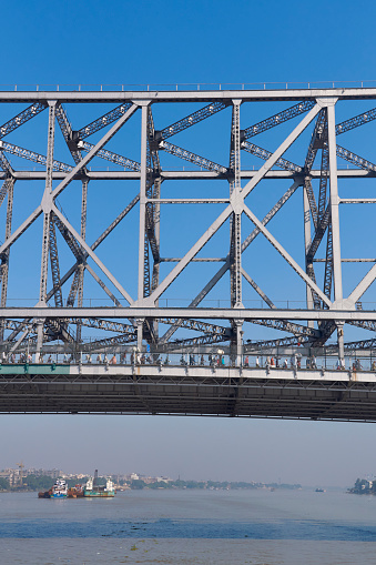 View of iconic Howrah Bridge (Rabindra Setu) of Kolkata over Ganges river, from a ferry boat. One of the world's busiest cantilever bridge, people are seen walking on the bridge. Everyday more than lakhs of people use this bridge which connects two cities, Howrah and Kolkata.