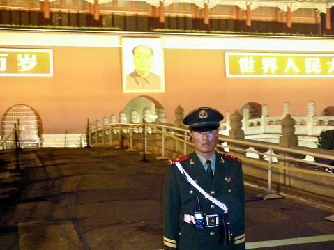 Beijing, China- April 11, 2008\n\nA military guard stands at attention in front of the Forbidden Palace Mao Zi Dong portrait at night. The background and portrait of Mao is washed out and blurred in orange light, creating artistic result.