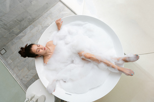 Asian beautiful young woman enjoying pleasant bath with foam, lying with closed eyes. Top viewHappy asian woman bathes with white foam in a bathtub fun emotions.