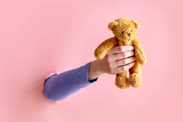 istock female hand hold teddy bear on pink background. 1309880479