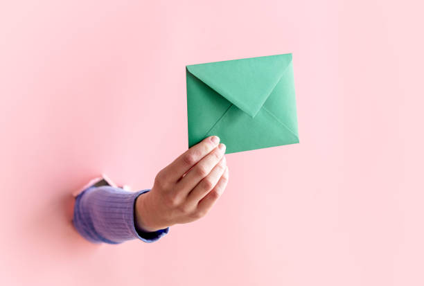 istock female hand hold green envelope on pink background. 1309880482
