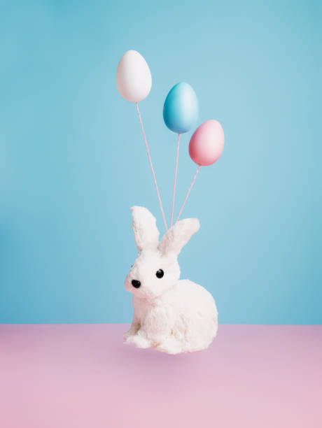 istock Painted egg helium balloons and rabbit flying and  floating against two tone pink and blue background. Creative art Easter concept. 1309883087