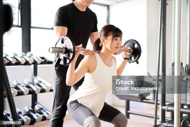 Asian Woman Doing Barbell Squats With The Assistance Of A Trainer Stock Photo - Download Image Now