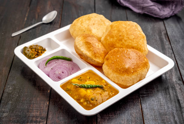 Masala Aloo Sabzi or Indian potato curry served with fried puri or Poori with sliced onion and mango pickle in a white plate Puri sabji - Indian semi dry Potato Spicy recipe also known as Batata or Aloo ki Sabji, served with fried Poori. It is a traditional breakfast dish in North India. Aloo Puri stock pictures, royalty-free photos & images