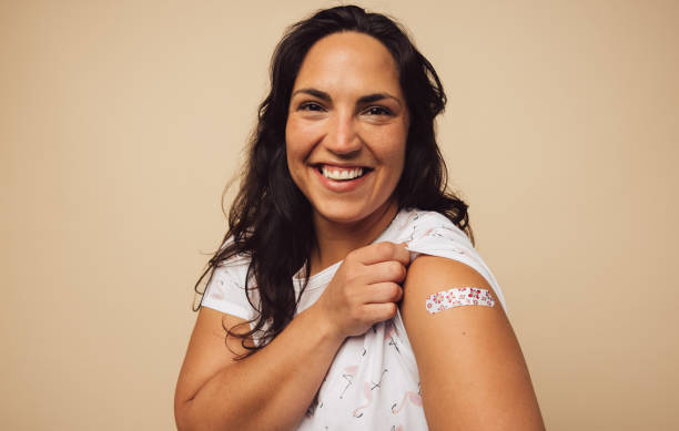 Woman feeling positive after getting vaccination Portrait of a female smiling after getting a vaccine. Woman holding up her sleeve and showing her arm with bandage after receiving vaccination. flu vaccine photos stock pictures, royalty-free photos & images
