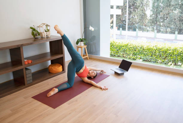 istock Young woman doing yoga on exercise mat at home, She is watching tutorials on laptop 1309891935