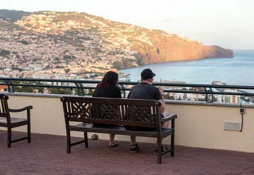 Funchal, Madeira, Portugal - September 13, 2016: the couple are sitting on a bench on the terrace and admiring the sunset over Funchal