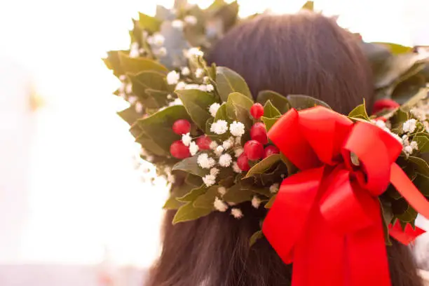 Graduate girl, with laurel wreath, flowers and red bow on her head celebrates.