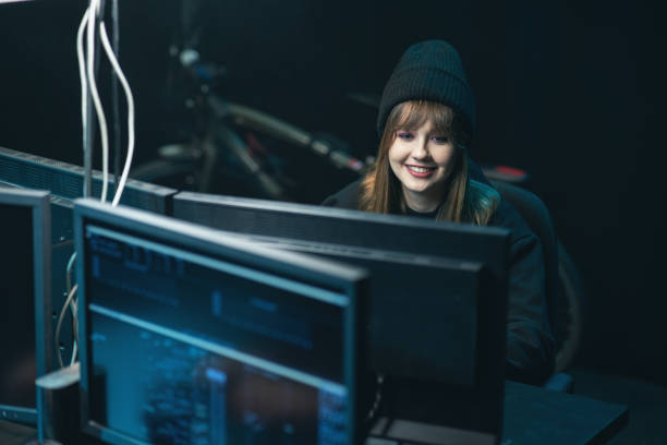istock Side view of Hooded Female Hacker Breaking into Corporate Data Servers from His Underground Hideout. Wanted anonymous programmer coding virus ransomware using computers 1309899471
