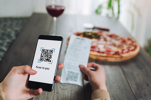 Women's hands using the phone to scan the qr code to pay pizza. Scan to get discounts or pay for pizza. The concept of using a phone to transfer money or paying money online without cash.FAKE QR.QR codes/barcodes in the image not contain offensive language, brand names, or links to websites or products.