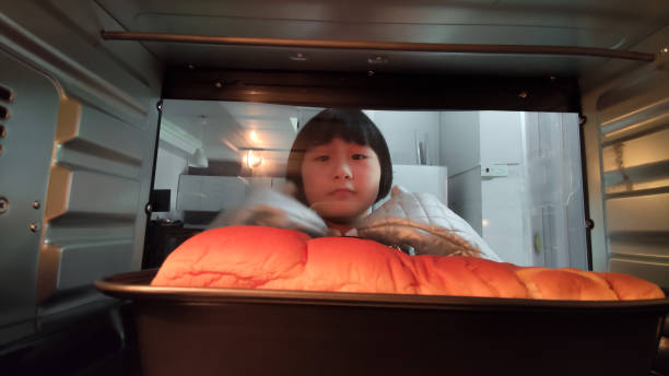 Asian Chinese girl waiting her baking bread food in the oven in the kitchen Asian Chinese girl waiting her baking bread food in the oven in the kitchen inside microwave stock pictures, royalty-free photos & images