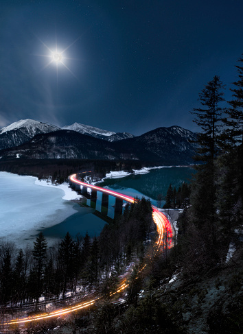 Road into the mountain at night - full moon with halo illuminating the scene