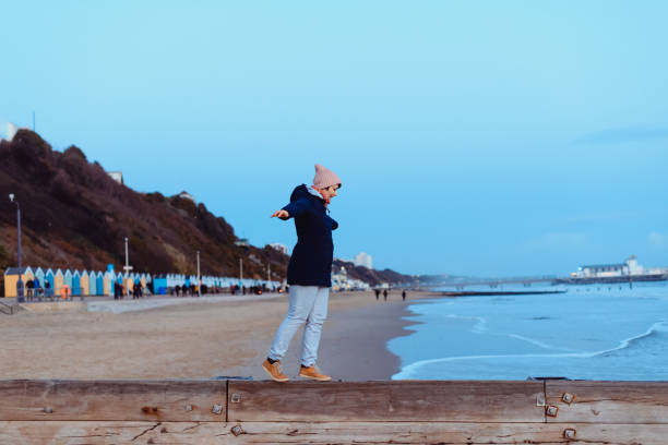 暖かい服を着た女性は、バランスを練習し、海岸の散歩中に瞬間と海の景色を楽しんでいます。リラックスして、個人的な充実。秋、冬に旅行。選択的フォーカス。コピースペース - winter women zen like photography ストックフォトと画像