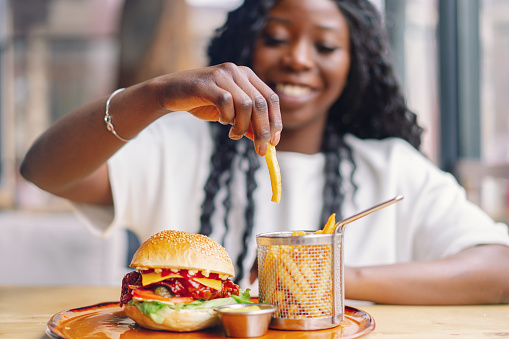 African woman with afro hair eating a tasty classic burger with fries. Cheat Meal.