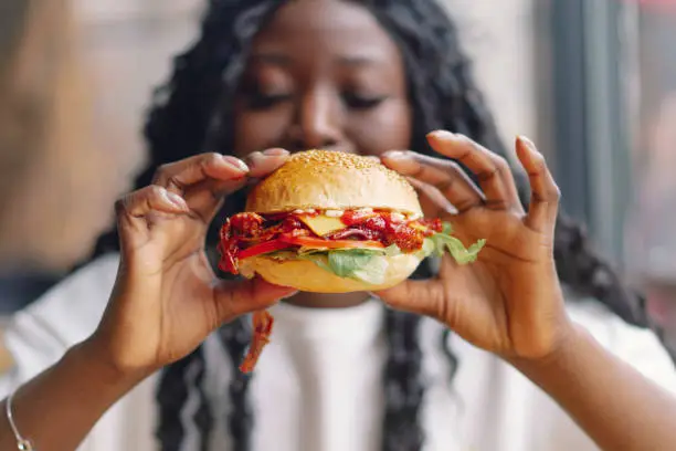 Photo of African woman with afro hair eating a tasty classic burger with fries.