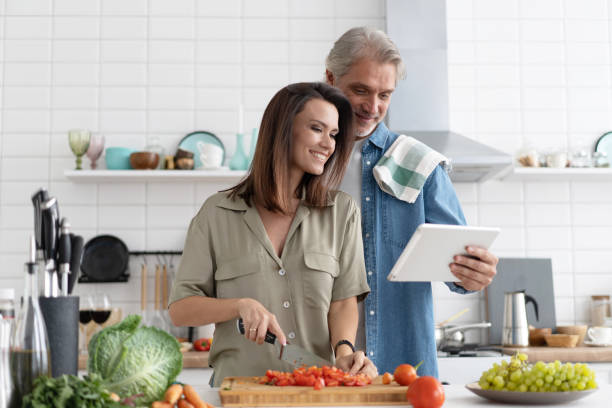 istock Beautiful couple using a digital tablet and smiling while cooking in kitchen at home. 1309915584
