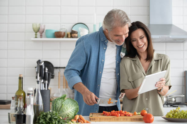 istock Beautiful couple using a digital tablet and smiling while cooking in kitchen at home. 1309915622