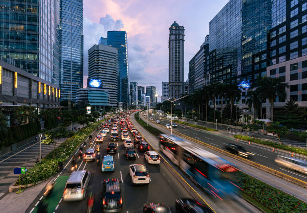 il traffico, catturato con movimento sfocato, si precipita lungo il viale principale fiancheggiato da grattacieli nel quartiere degli affari nella capitale indonesiana. - indonesia foto e immagini stock