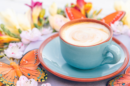 Bright blue cup with creamy coffee in boho style with freesias, cherry blossoms and butterflies. Added grain. Part of a series.