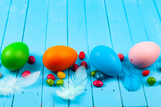 Eggs, candies and feathers on a blue wooden background, place for your text. Easter still life.