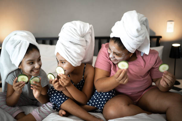 Morther and daughters in bed doing skin care holding cucumber slices Morther and daughters in bed doing skin care holding cucumber slices women facial mask mud cucumber stock pictures, royalty-free photos & images