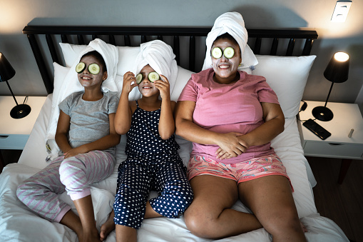Morther and daughters in bed doing skin care with cucumber slices over the eyes