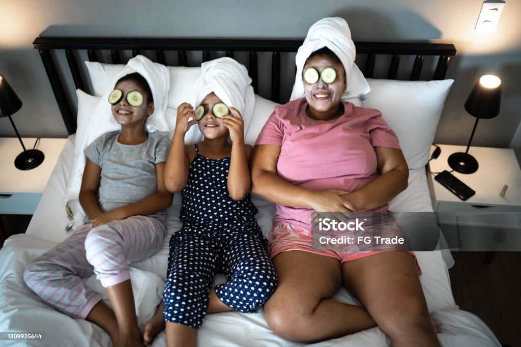 Morther and daughters in bed doing skin care with cucumber slices over the eyes Relaxation Stock Photo