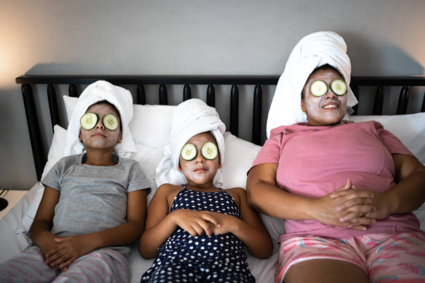 Morther and daughters in bed doing skin care with cucumber slices over the eyes Morther and daughters in bed doing skin care with cucumber slices over the eyes women facial mask mud cucumber stock pictures, royalty-free photos & images