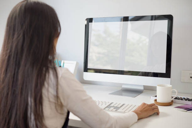 istock Mockup blank white desktop screen computer with a woman working in background. White screen computer for graphic montage. clipping path 1309927987