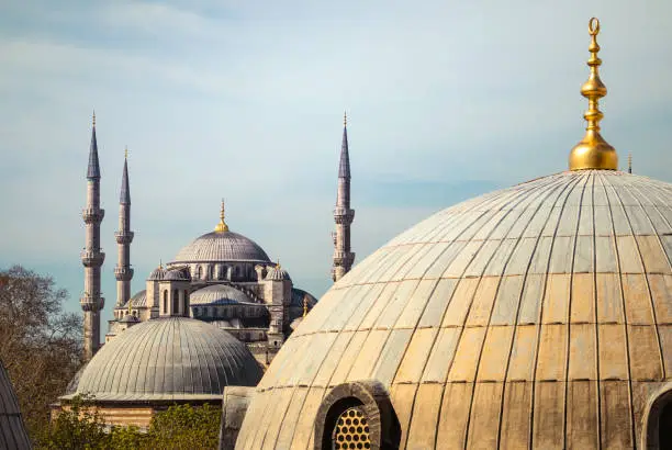 Blue Mosque or Sultanahmet Camii Mosque in Istanbul. View of the ancient Turkish temple with minarets through the window of the Hagia Sophia with church dome, a golden spire and arabian symbol on the top.