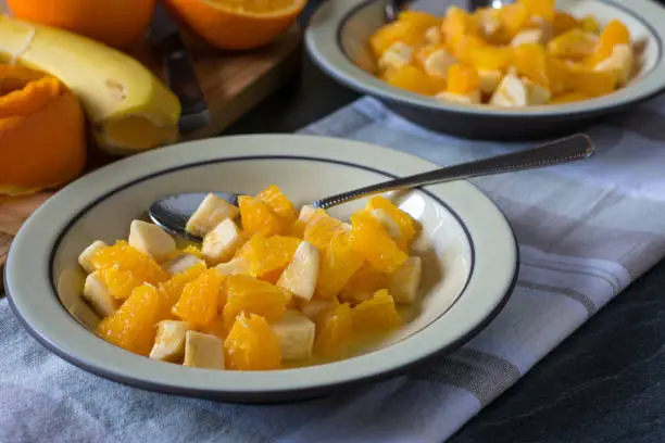 Delicious and healthy fruit salad with chopped bananas and oranges served on a plate on kitchen table