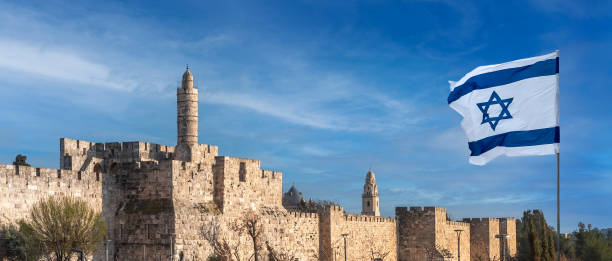 Tower of David with Israeli flag, panoramic view. Panorama of Jerusalem's Citadel near the Jaffa Gate with Tower of David, ancient fortress walls and Israeli flag. Zion Mount with buildings of Dormition Abbey and bell tower on background. holy site stock pictures, royalty-free photos & images