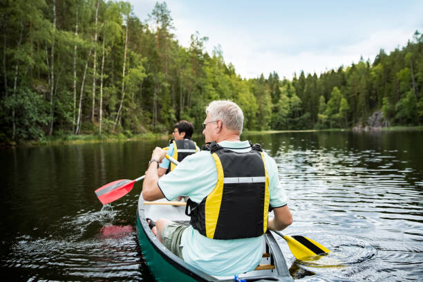 feliz pareja madura en chalecos salvavidas piragüismo en el lago del bosque - finland lake summer couple fotografías e imágenes de stock