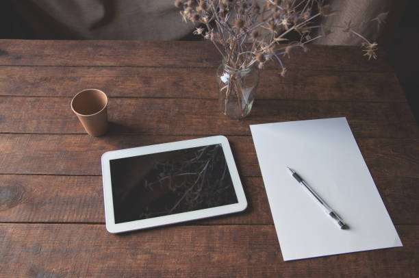 lieu de travail moderne de bureau avec le pc de tablette sur la table. sur la table est un ordinateur tablette avec une feuille de papier blanc, des fleurs séchées dans un verre et une tasse de café jetable. - book school desk old photos et images de collection