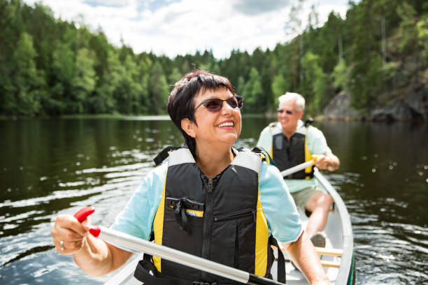 feliz pareja madura en chalecos salvavidas piragüismo en el lago del bosque - finland lake summer couple fotografías e imágenes de stock