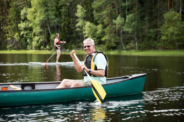 feliz pareja madura en chalecos salvavidas piragüismo en el lago del bosque - finland lake summer couple fotografías e imágenes de stock