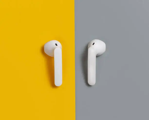 White wireless earphones on yellow and grey background  top view