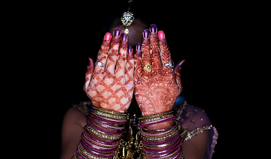 Traditional Indian woman hiding behind henna hand and she standing against black background.