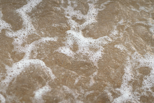 A wave with foam running onto the shore covered with small pebbles, close-up, top view