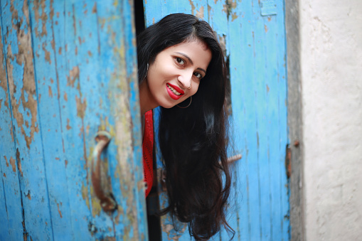 Beautiful young Indian female peeking from old wooden door.