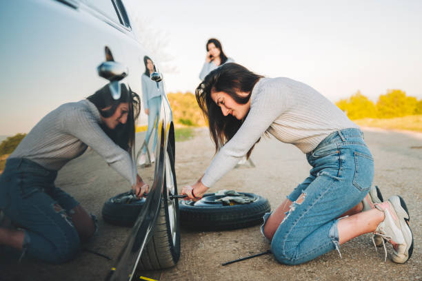Desperate young woman trying to change a flat tire with tire iron on the road Woman changing wheel after a car breakdown at the side of the road. Transportation, traveling concept. She looks tired and desperate, and waiting help from someone flat tire stock pictures, royalty-free photos & images