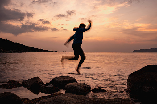 Silhouette of man jumping on air with beautiful sunset on the sea. Long exposure shot with motion blur..