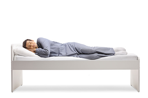 Full length shot of a man sleeping peacefully in a single bed isolated on white background