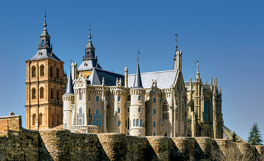 View of landmark cathedral of Astorga, Spain, and historic Gaudi building behind ancient Roman surrounding wall.