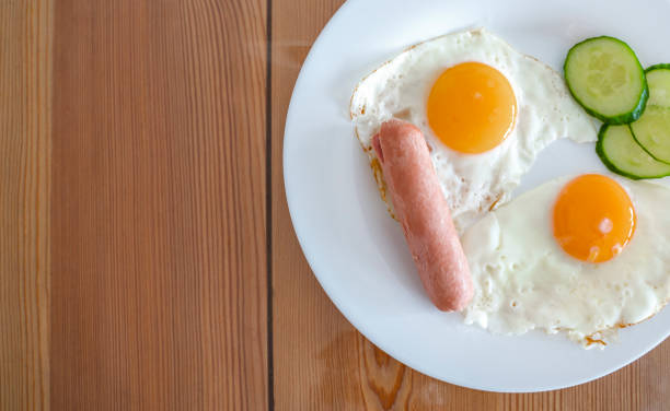 istock Fried eggs from two eggs with cucumbers and sausage for breakfast. Fried eggs, sunny side up on a plate. Healthy food concept. 1309948115